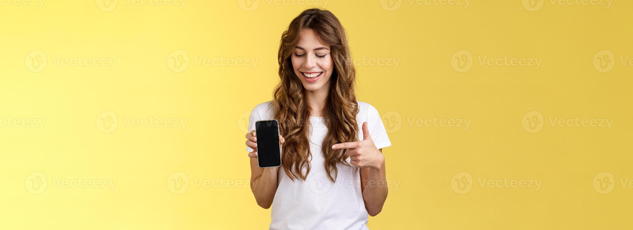 intrigado carismático feliz jovem fêmea blogueiro mostrar o que foto aplicativo usar editar social meios de comunicação perfil aguarde Smartphone olhando apontando índice dedo Móvel telefone em branco tela sorridente divertido