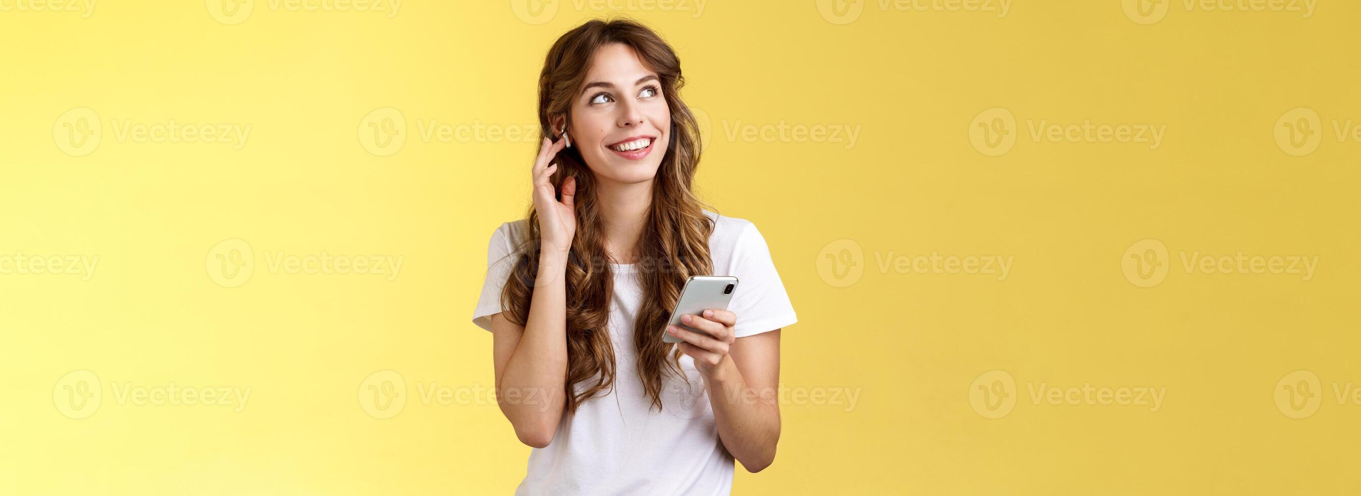 sonhadores feliz alegre cabelo encaracolado menina Veja por aí contemplar lindo verão clima ouvindo música toque sem fio fone de ouvido chamando amigo falando através da fones de ouvido aguarde Smartphone amarelo fundo foto