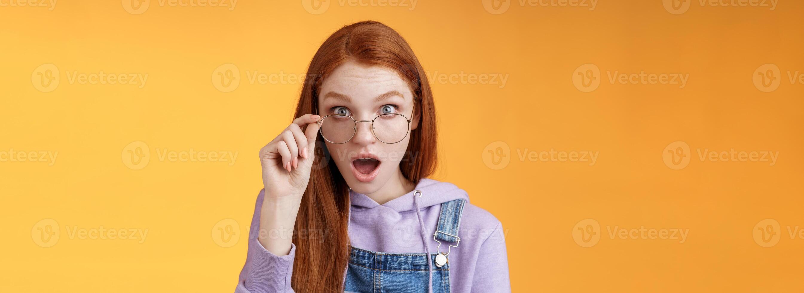 chocado impressionado ruiva colega de trabalho audição último íntimo rumores solta mandíbula encarando cheio descrença Câmera confuso toque óculos parecer inseguro verdade mentira em pé laranja fundo atônito foto