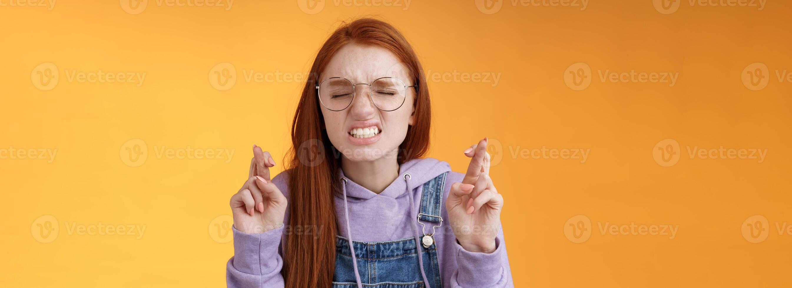 menina desejos ganhar inferior coração suplicante sério apertar dentes franzindo a testa fechar olhos implorando senhor Cruz dedos Boa sorte Rezar fazer sério desejo em pé laranja fundo Sonhe venha verdade foto