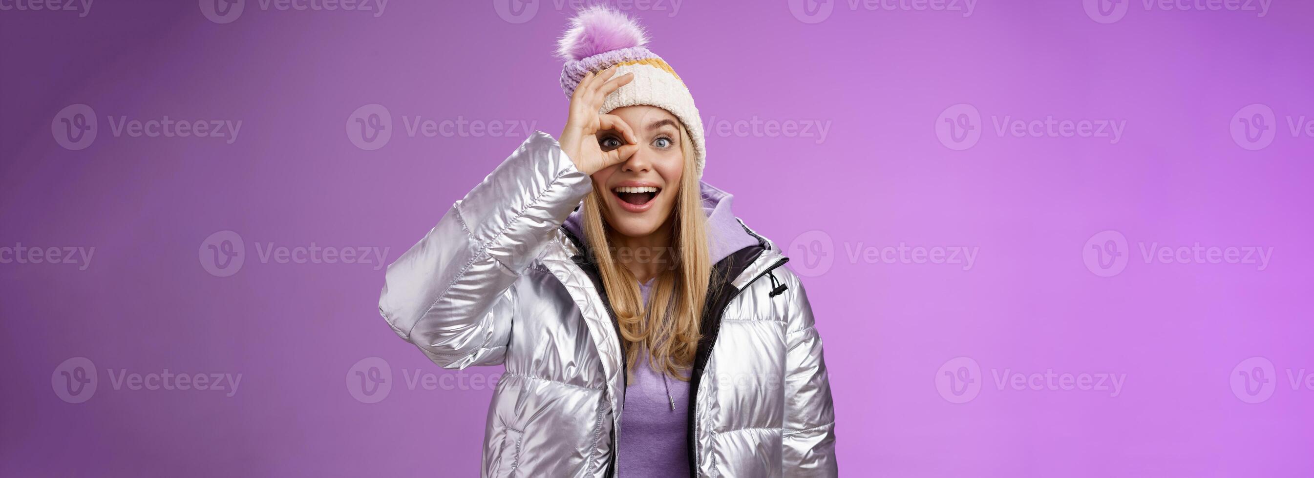 impressionado curioso boa aparência loiro à moda fêmea viajante Encantado Nevado montanhas Visão aguarde OK Está bem placa olho sorridente atônito sem palavras observando lindo cenário dentro brilhante prata Jaqueta chapéu foto