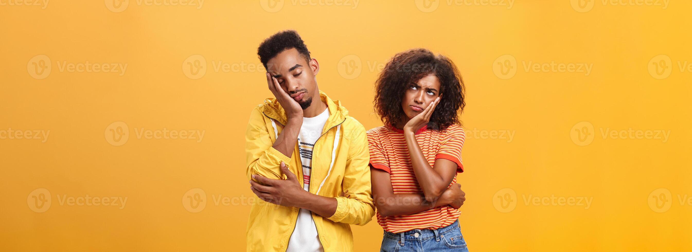 menina sentindo-me descontente e ofendido em namorado quem caiu adormecido durante encontro perseguindo lábios franzindo a testa olhando acima enquanto namorado inclinado cabeça em face com fechadas olhos e cansado Veja sobre laranja parede foto