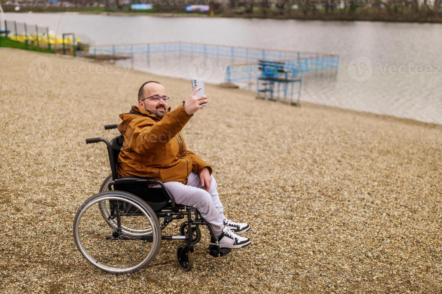 paraplégico deficiente homem dentro cadeira de rodas é levando selfie com Smartphone ar livre. foto