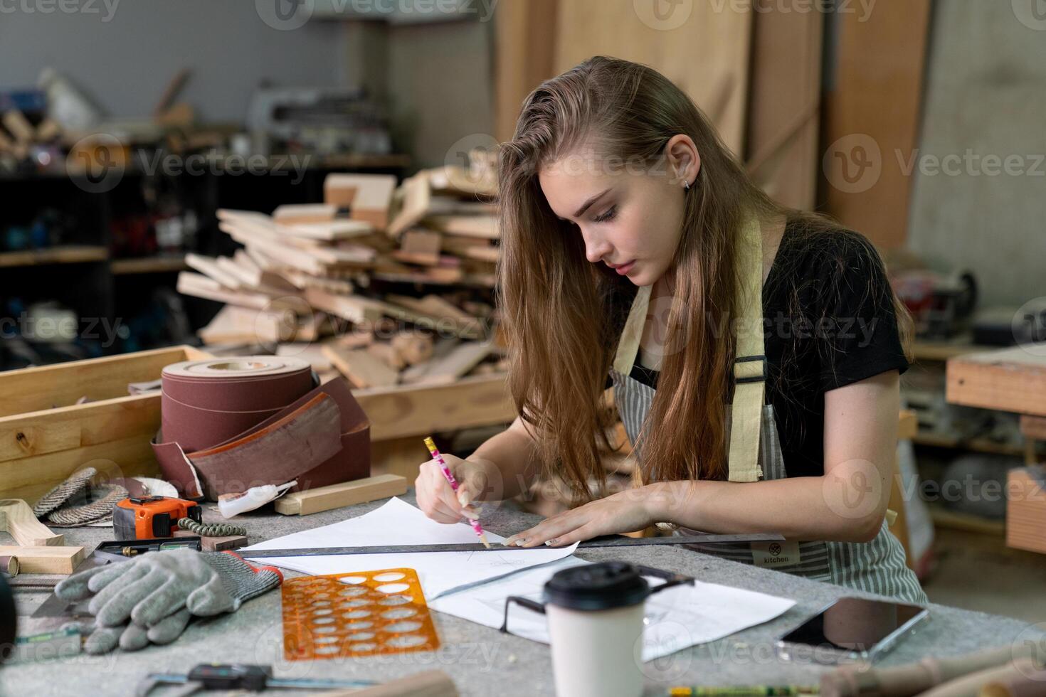 uma jovem mulher é Treinamento para estar uma carpinteiro dentro a oficina. ela trabalho com uma computador portátil computador dentro uma madeira oficina. fêmea carpinteiro contato clientes de Smartphone. sme foto