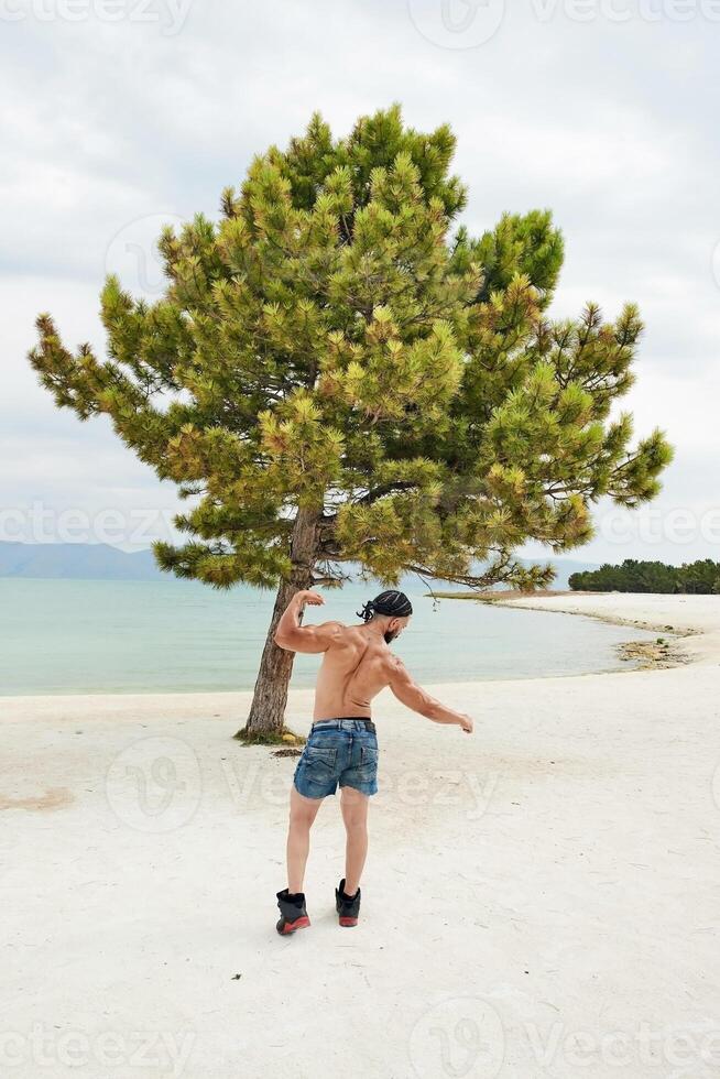 jovem muscular homem exercício em a praia, jovem muscular homem fazendo musculação exercícios em a praia, Atlético jovem homem em a de praia foto