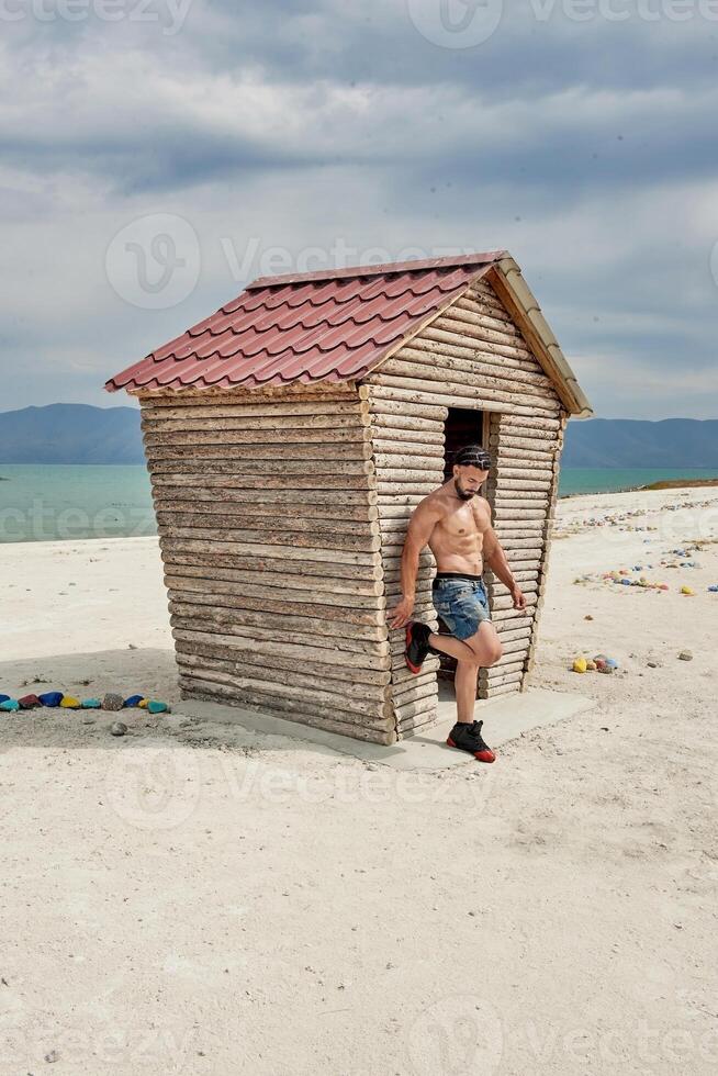 jovem muscular homem exercício em a praia, jovem muscular homem fazendo musculação exercícios em a praia, Atlético jovem homem em a de praia foto