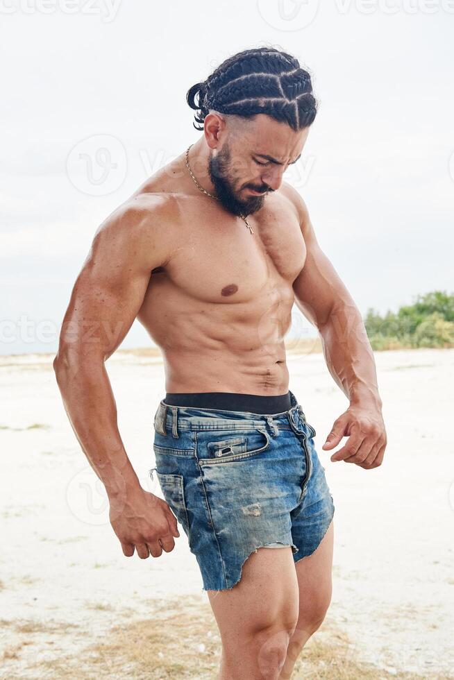 jovem muscular homem exercício em a praia, jovem muscular homem fazendo musculação exercícios em a praia, Atlético jovem homem em a de praia foto