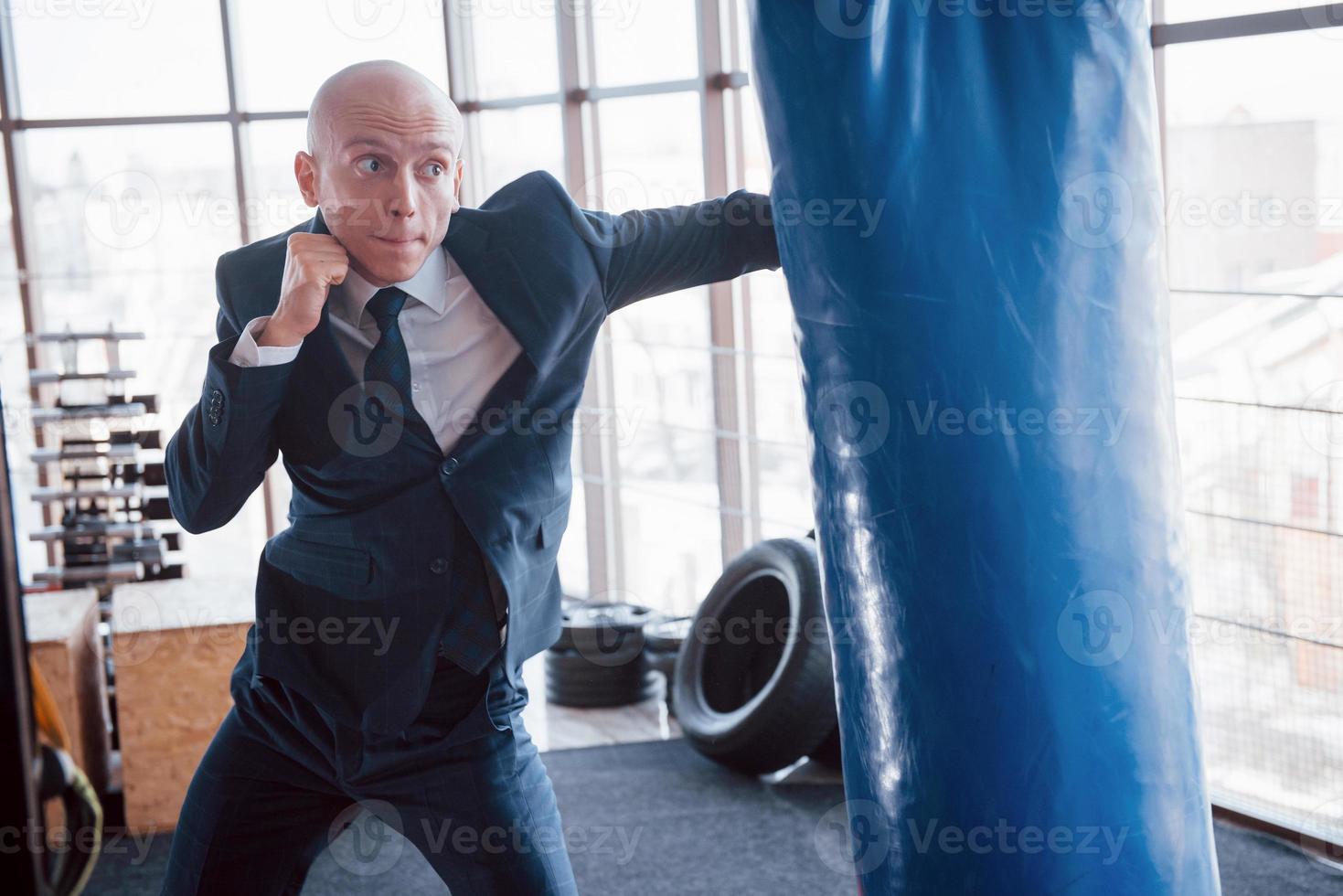 um empresário careca zangado derrota uma pêra de boxe no ginásio. conceito de gerenciamento de raiva foto