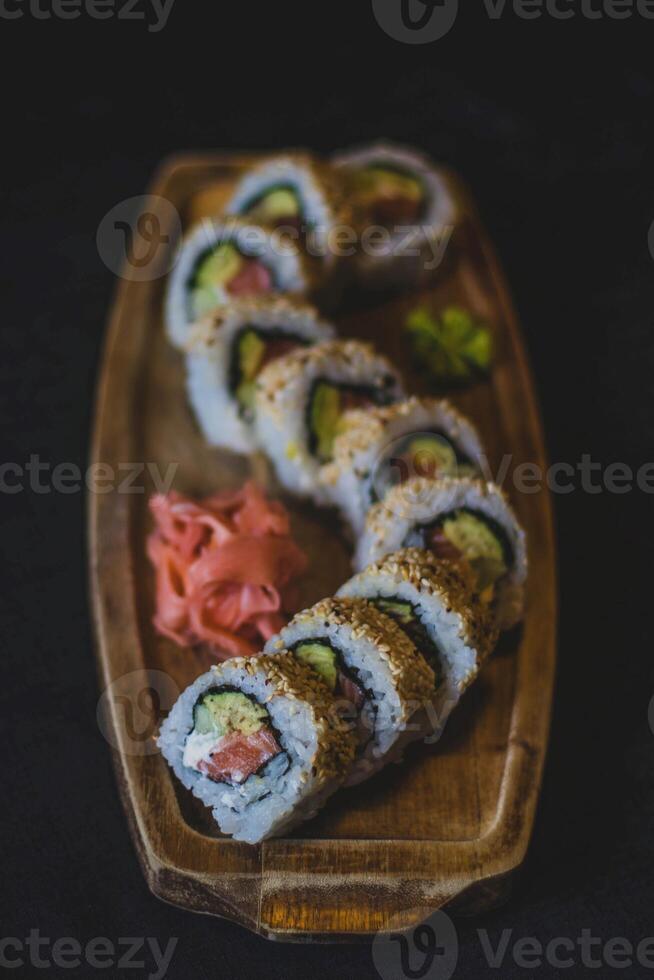 Sushi rolos em uma de madeira prato em uma Preto fundo. japonês Comida foto