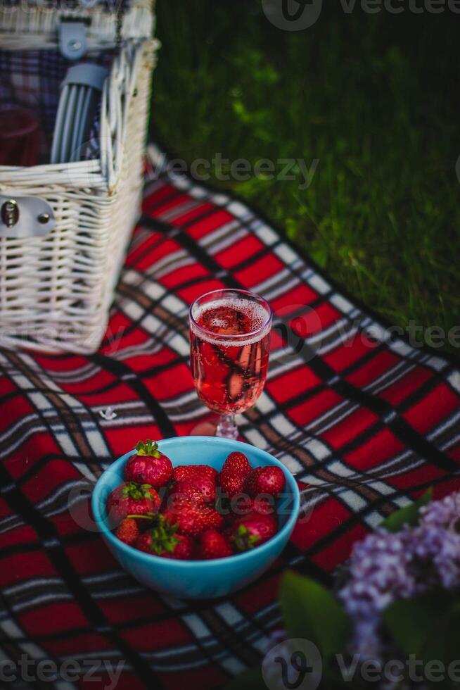 morangos dentro uma tigela e uma vidro do rosa vinho em uma piquenique cobertor foto