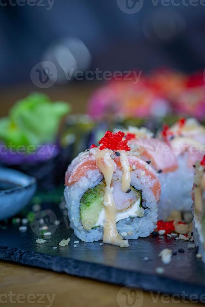 Sushi rolos em uma Preto prato em uma de madeira mesa dentro uma restaurante foto
