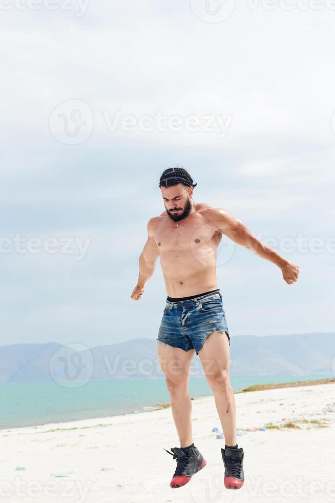 jovem muscular homem exercício em a praia, jovem muscular homem fazendo musculação exercícios em a praia, Atlético jovem homem em a de praia foto