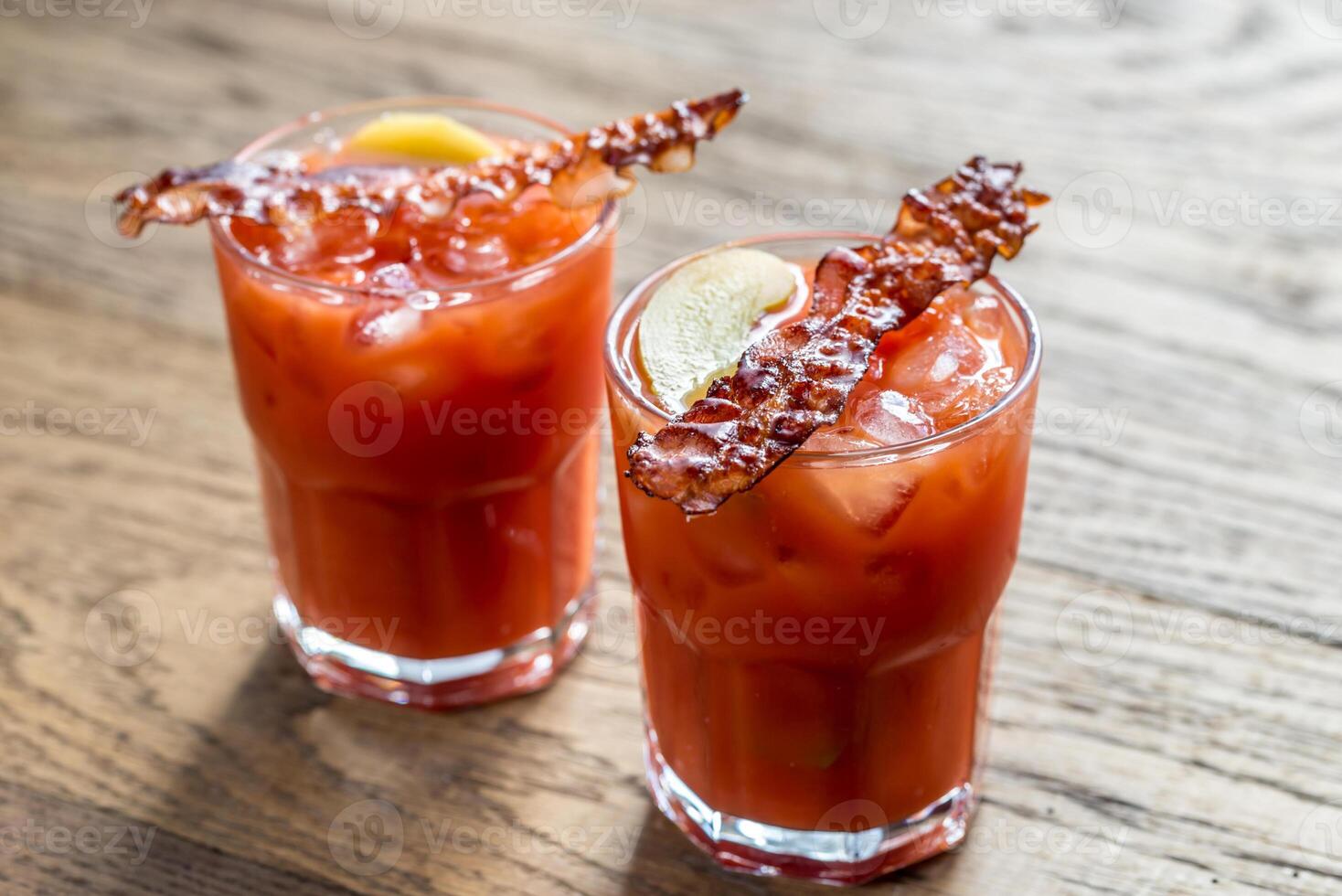 dois copos de bloody mary com fatias de bacon foto