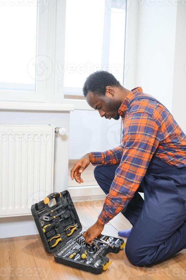 reparar aquecimento radiador fechar-se. africano homem reparação radiador com chave inglesa. removendo ar a partir de a radiador foto