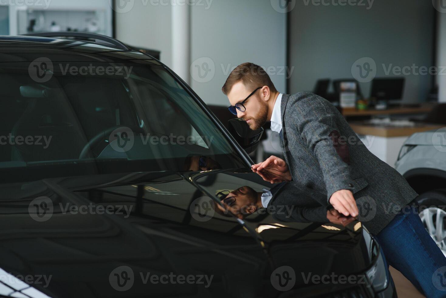 visitando carro concessionária. bonito barbudo homem é acariciando dele Novo carro e sorridente foto