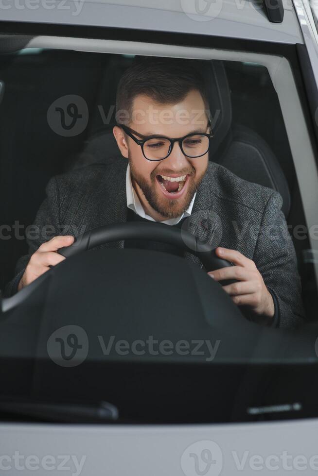 visitando carro concessionária. bonito barbudo homem é acariciando dele Novo carro e sorridente foto