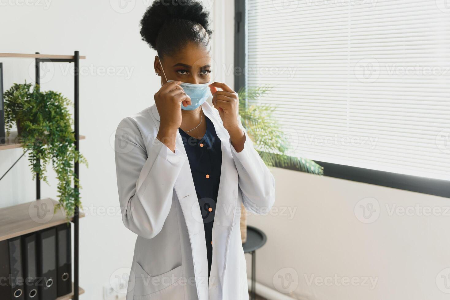 medicamento, profissão e cuidados de saúde conceito - africano americano fêmea médico ou cientista dentro protetora facial mascarar dentro clínica. foto