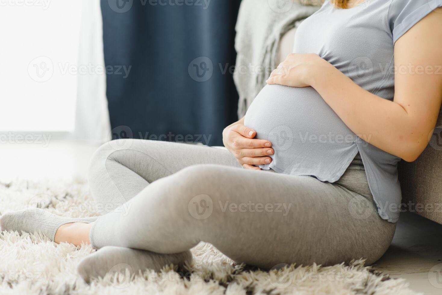 grávida mulher fazendo carinho dela barriga às lar. jovem expectante Loiras sentindo-me dela bebê empurrar, sentado em chão, cópia de espaço. gravidez, descansar, vida, expectativa conceito foto