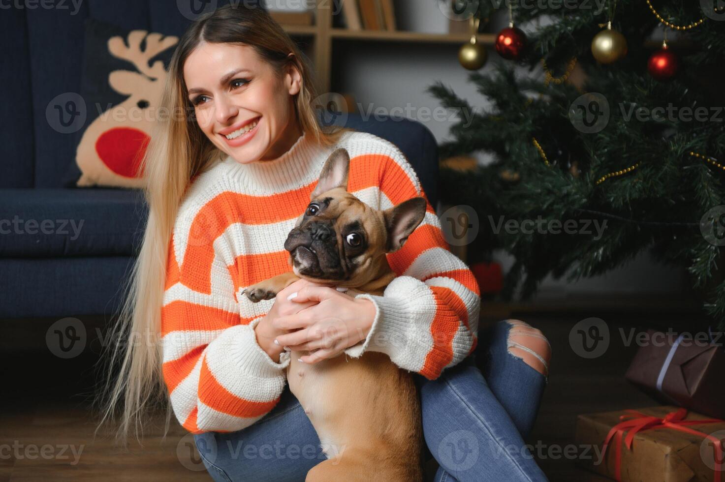 lindo mulher senta em uma vintage sofá com cachorro. em uma fundo do uma Natal árvore dentro uma decorado sala. feliz Novo ano foto