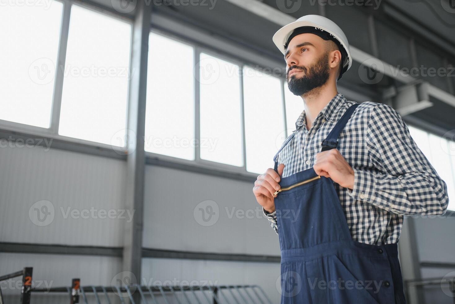 retrato do profissional pesado indústria engenheiro trabalhador vestindo segurança uniforme, Difícil chapéu sorridente. dentro a fundo desfocado ampla industrial fábrica. foto