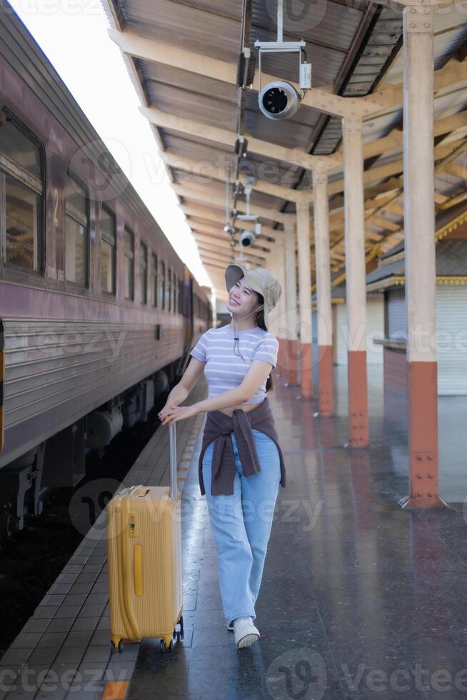 jovem mulher com mala de viagem espera às a metro estação enquanto a trem chega, turismo e viagem dentro a verão. Férias para a estudante. trabalhos e viagem foto