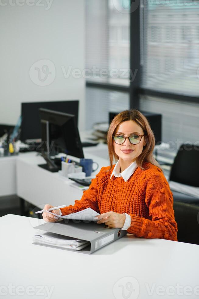 retrato do uma feliz casual empresária dentro suéter sentado às dela local de trabalho dentro escritório foto