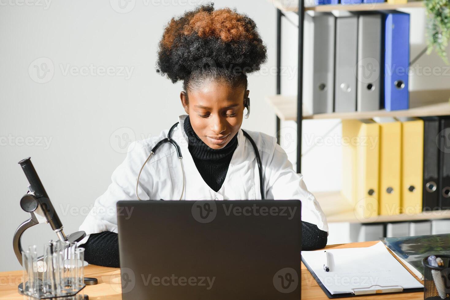 sorridente africano americano fêmea médico gp desgasta branco médico casaco usando computador portátil computador às local de trabalho dá controlo remoto conectados consulta, trabalhando em pc, consultando paciente dentro Internet telemedicina bate-papo foto