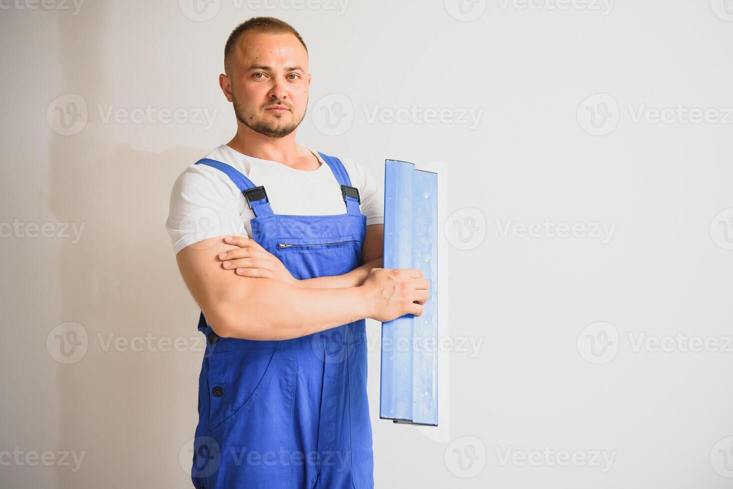 retrato do uma trabalhador dentro macacão e segurando uma massa de vidraceiro faca dentro dele mãos contra a gesso parede fundo. reparar trabalhos e construção conceito foto