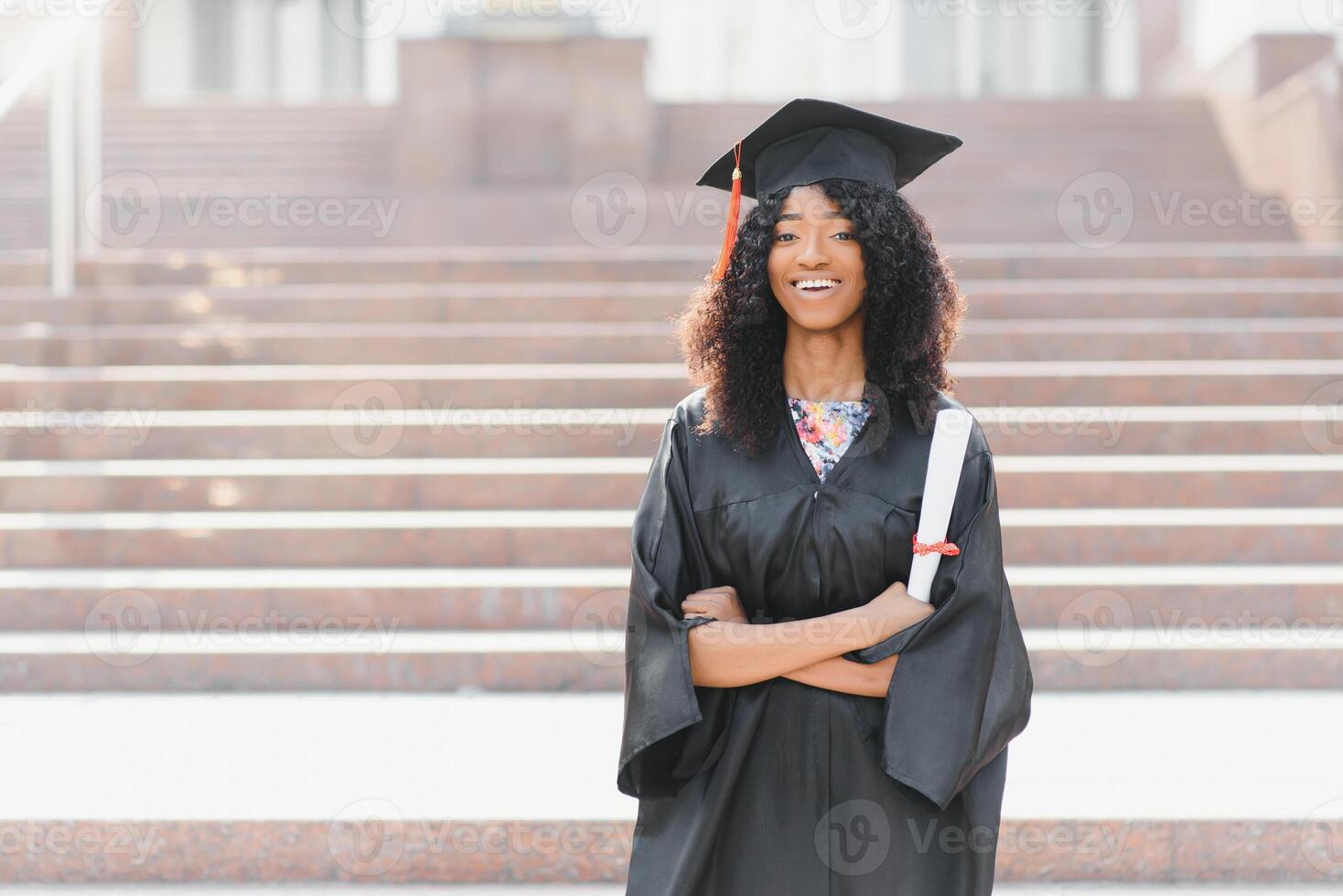 alegre afro americano fêmea graduado em pé dentro frente do universidade construção foto