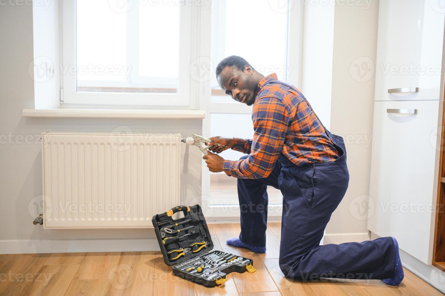homem dentro vestuário de trabalho macacão usando Ferramentas enquanto instalando ou reparação aquecimento radiador dentro quarto foto