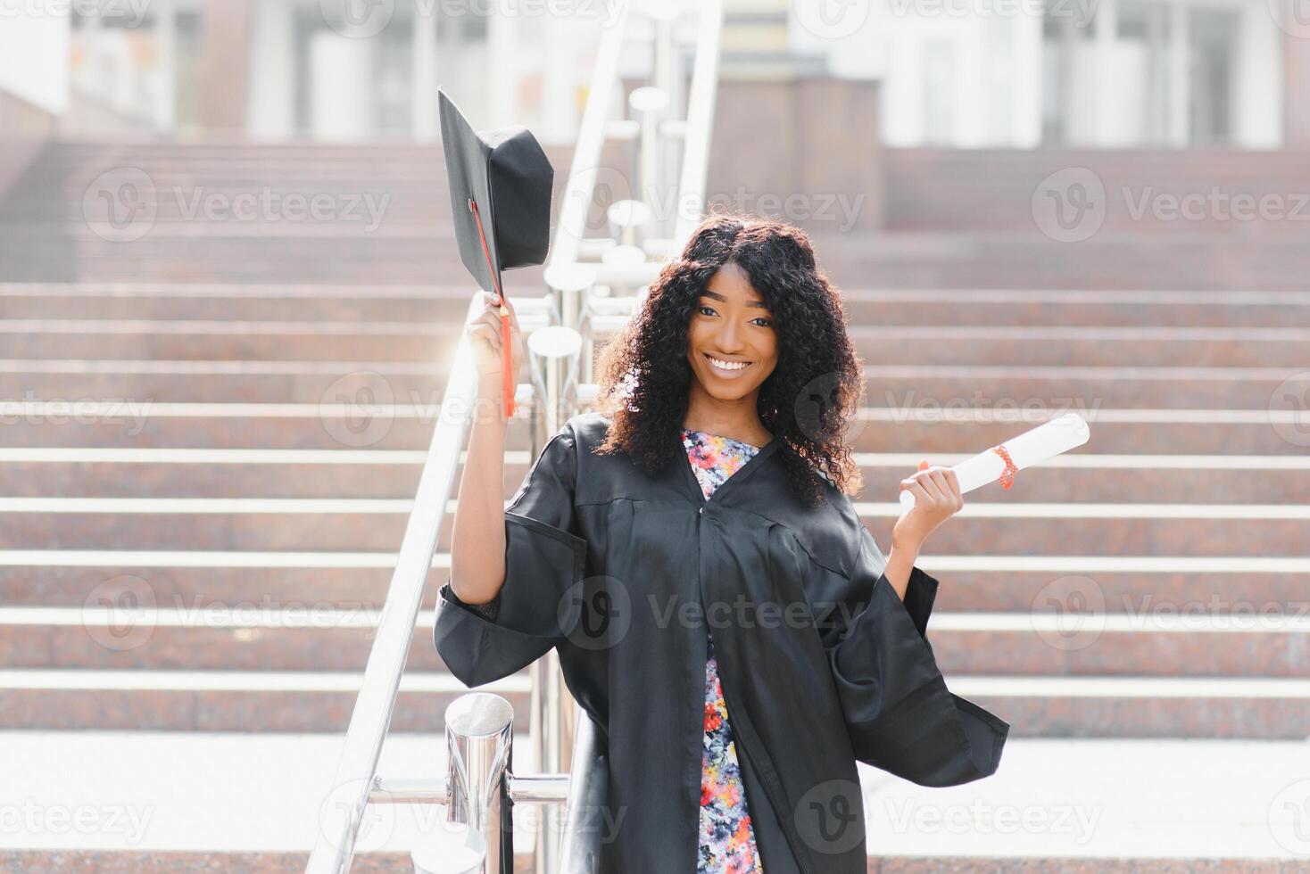 alegre afro americano fêmea graduado em pé dentro frente do universidade construção foto