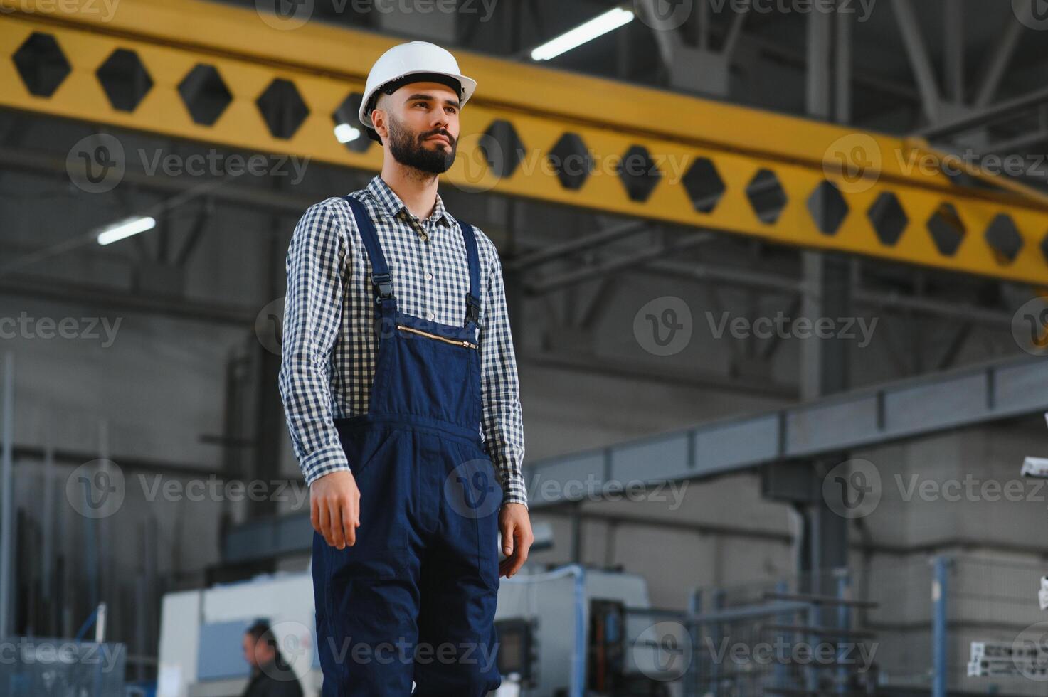 retrato do profissional pesado indústria engenheiro trabalhador vestindo segurança uniforme, Difícil chapéu sorridente. dentro a fundo desfocado ampla industrial fábrica. foto