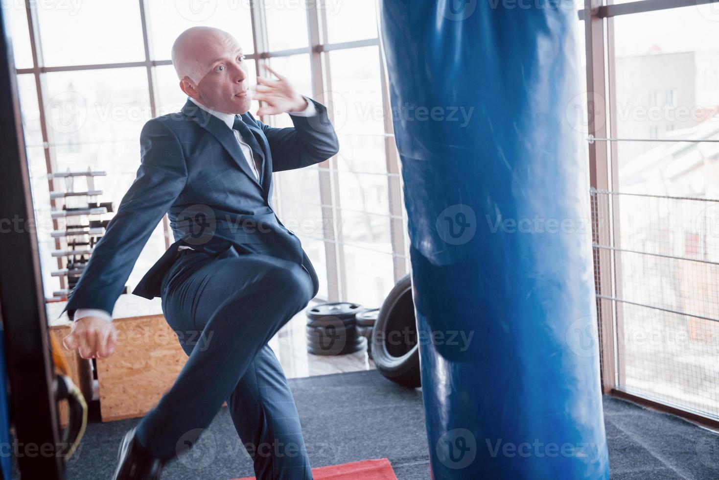 um empresário careca zangado derrota uma pêra de boxe no ginásio. conceito de gerenciamento de raiva foto