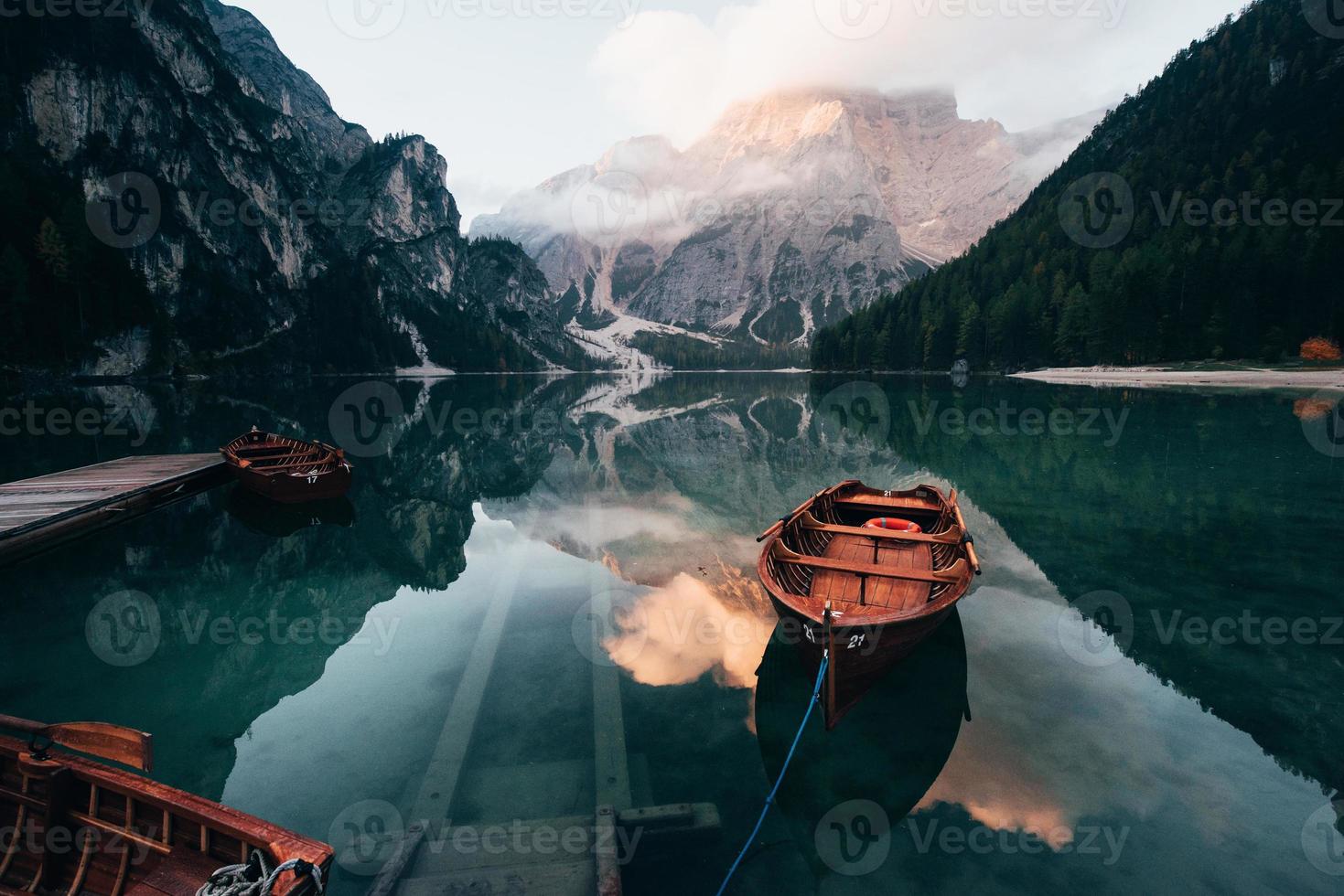 esperando pelos visitantes. barcos de madeira no lago de cristal com majestosa montanha atrás. reflexo na água foto