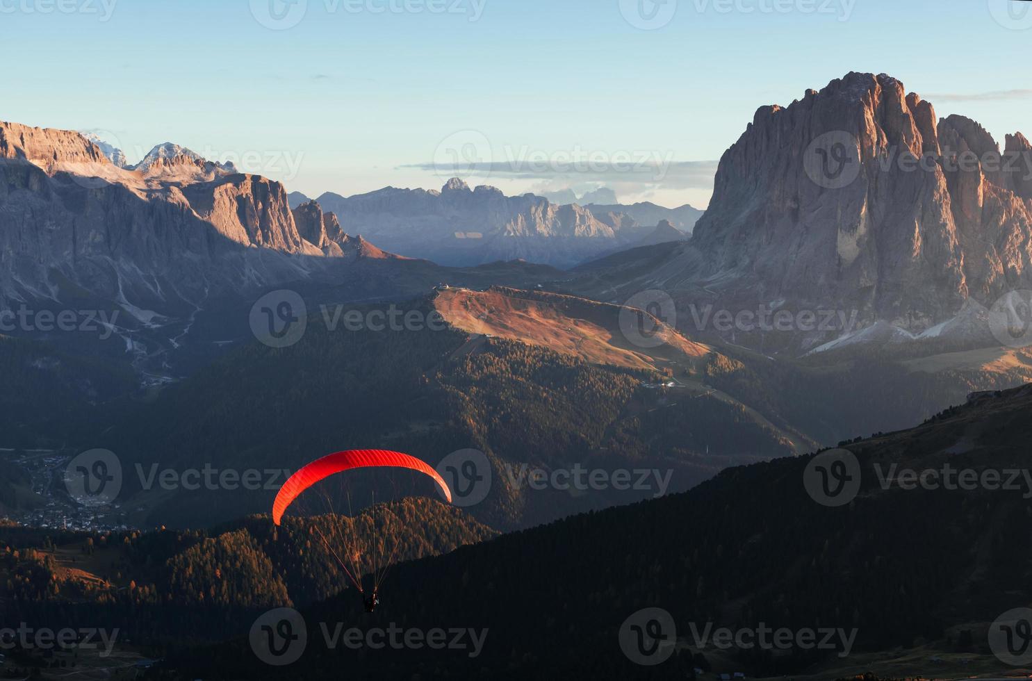 parapente com pára-quedas vermelho voa sobre as montanhas cheias de árvores ao sol foto