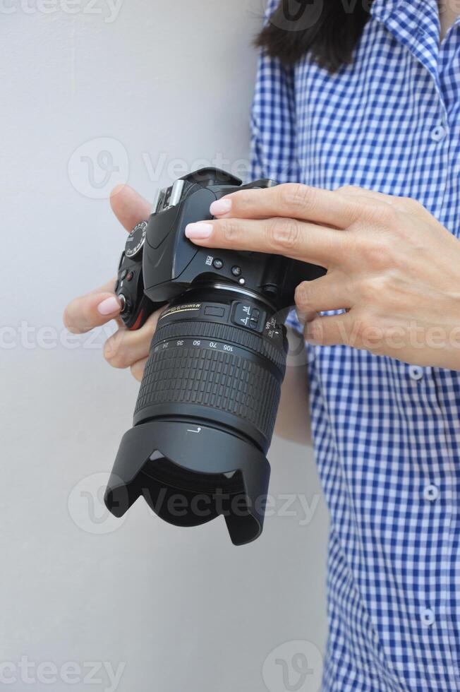 profissional Câmera dentro fêmea mãos. uma menina fotógrafo dentro uma azul camisa detém uma Câmera, parece através uma foto e Verificações a configurações antes tiroteio.