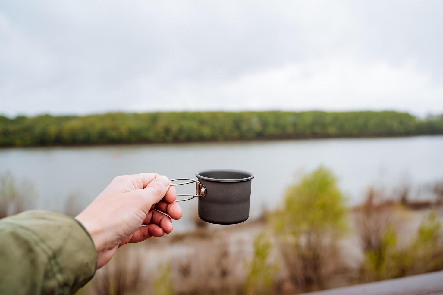 café caneca para acampamento dentro natureza, homem mão segurando uma caneca, chá vidro, metal copo para quente bebidas, alumínio utensílios foto