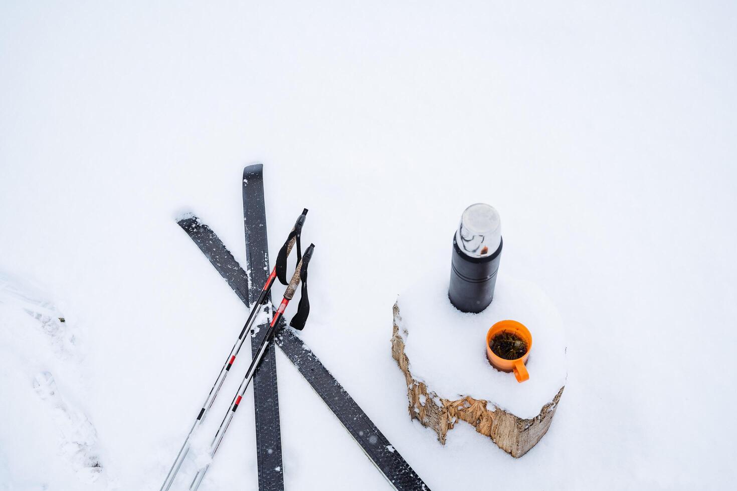 falso postes e esquis mentira em a neve, Próximo para uma toco com uma garrafa térmica e uma caneca do chá. inverno ainda vida dentro a neve. esquiar dentro a bosques, fresco ar foto