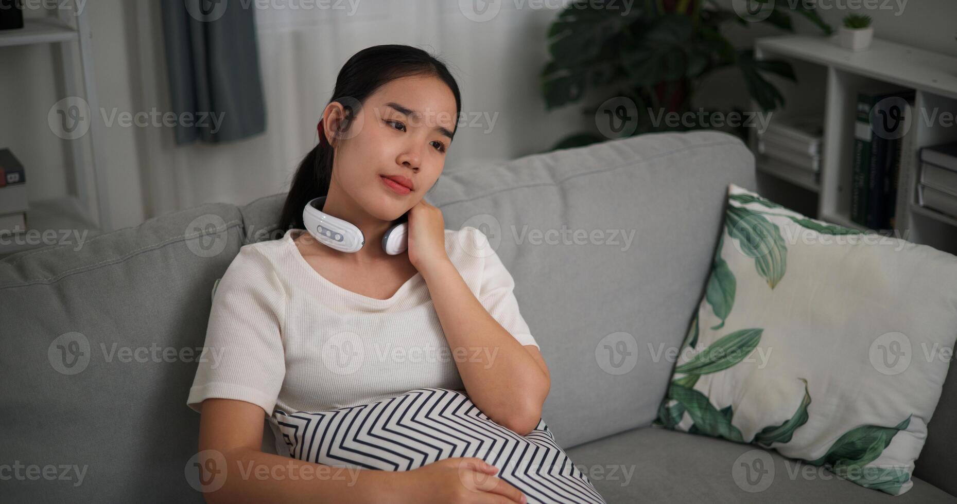 Alto ângulo visualizar, relaxado jovem mulher vestem automático massagem pescoço sentado em sofá às casa ,relaxante corpo e mente sozinho dentro a vivo sala, respiração fresco ar, foto