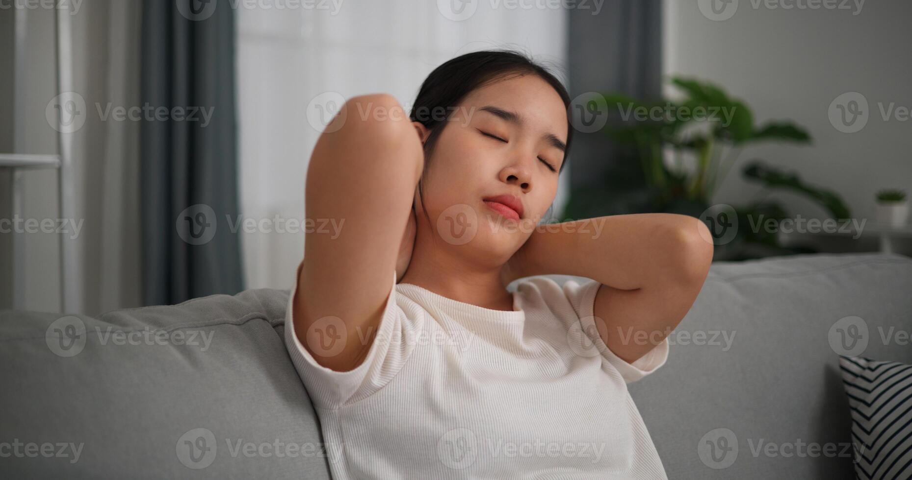 seletivo foco, feliz jovem mulher é praticando ioga e alongamento dela pescoço às casa com olhos fechado, relaxante corpo e mente sozinho em sofá dentro a vivo quarto, relaxamento estilo de vida foto