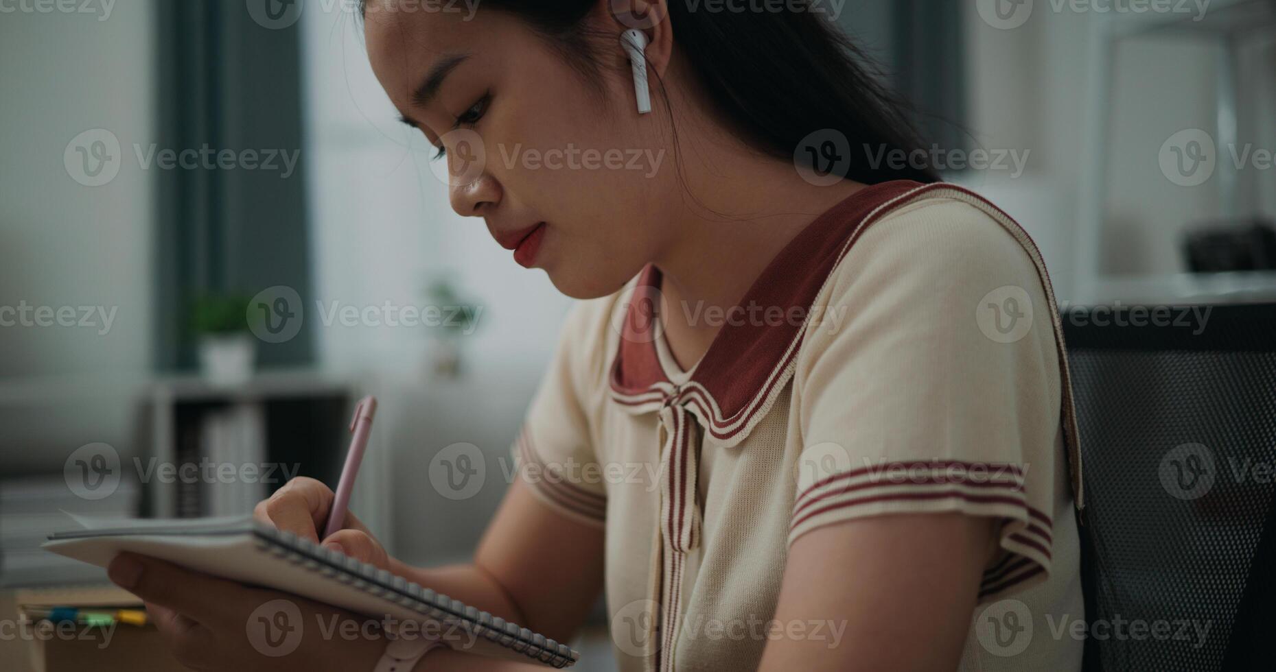 seletivo foco, lado visualizar, fêmea escritor vestem sem fio fones de ouvido sentado às escrivaninha enquanto escrevendo notas às lar, criativo pensamentos para diário, idéia e inspiração foto