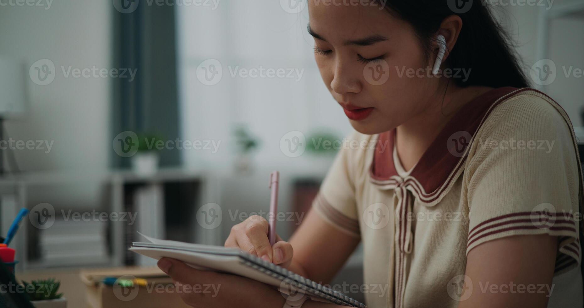 seletivo foco, lado visualizar, fêmea escritor vestem sem fio fones de ouvido sentado às escrivaninha enquanto escrevendo notas às lar, criativo pensamentos para diário, idéia e inspiração foto