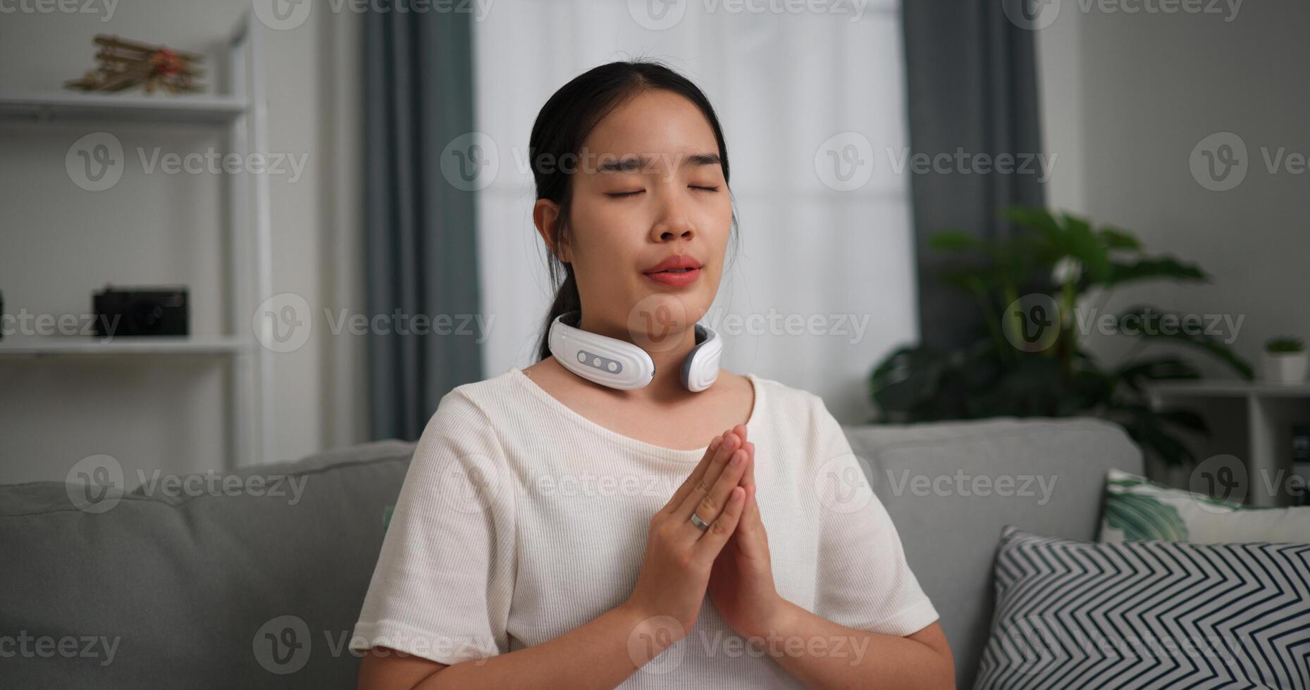 seletivo foco, relaxado jovem mulher vestem automático massagem pescoço com olhos fechado, sentado em sofá às casa ,relaxante corpo e mente sozinho dentro a vivo sala, respiração fresco ar, foto
