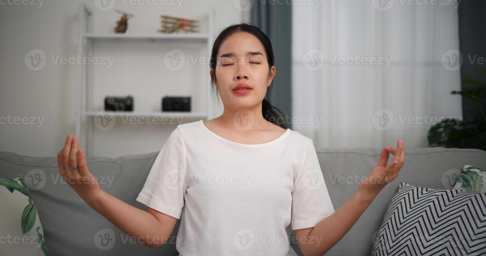 seletivo foco, feliz jovem mulher meditando fazendo uma lótus pose às casa com olhos fechado, relaxante corpo e mente sozinho em sofá dentro a vivo quarto, relaxamento estilo de vida foto