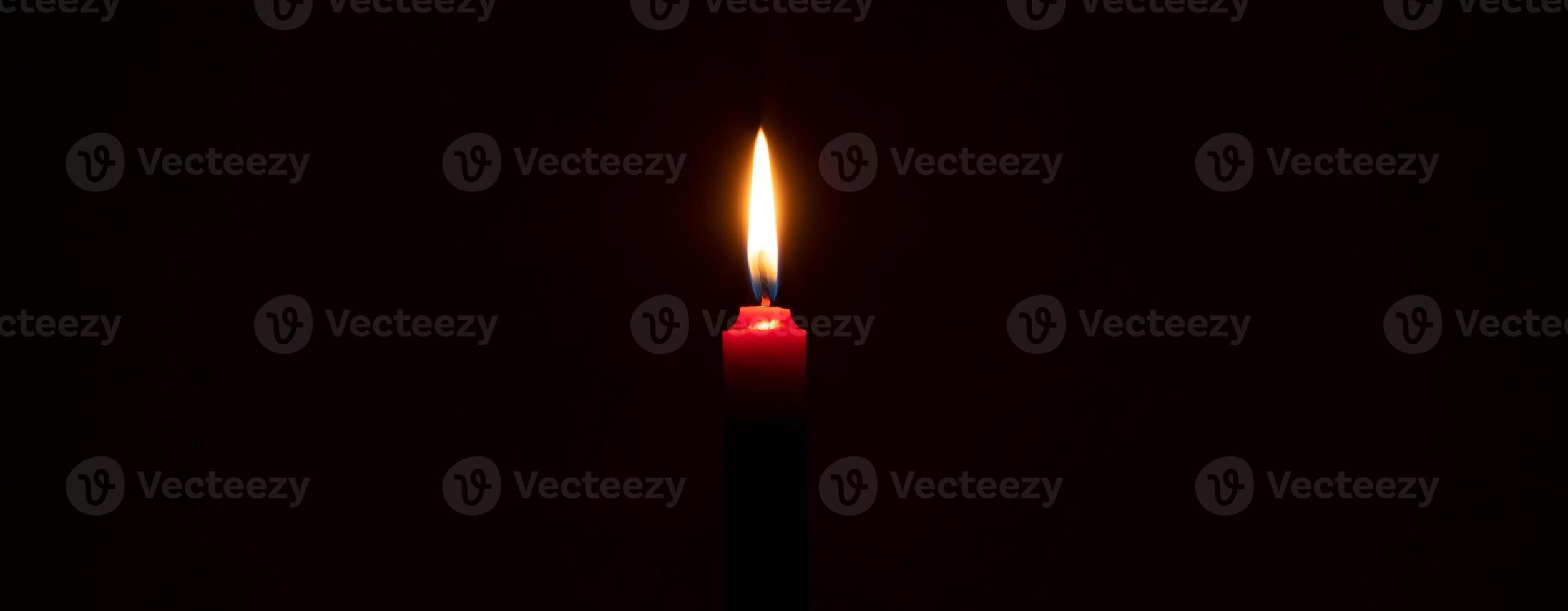 solteiro queimando vela chama ou luz brilhando em uma pequeno vermelho vela em Preto ou Sombrio fundo em mesa dentro Igreja para Natal, velório ou memorial serviço com cópia de espaço foto
