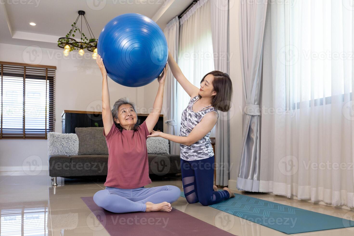 Senior ásia mulher é exercício às casa usando ioga bola para testemunho corpo e abdômen músculo construção com dela treinador filha ajustando a pose e encorajar para mais velho saudável foto