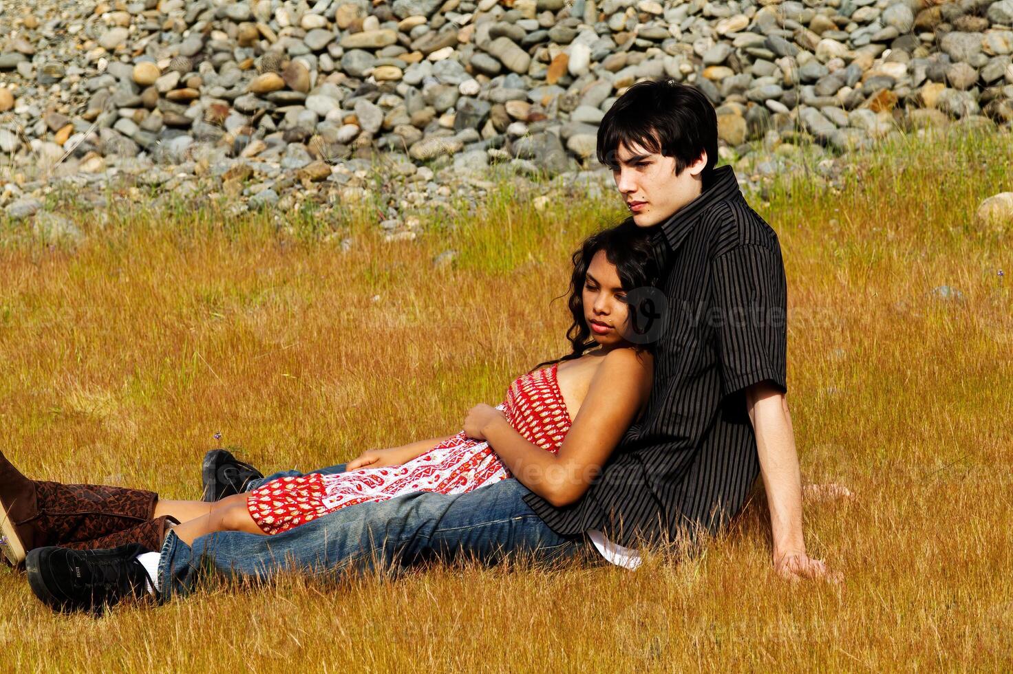 jovem adolescente casal sentado dentro Relva com pedras dentro fundo foto