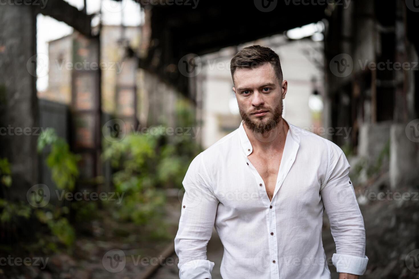 moda e à moda jovem masculino posando em quebrado construção fundo. bonito homem dentro branco camisa olhando às a Câmera foto