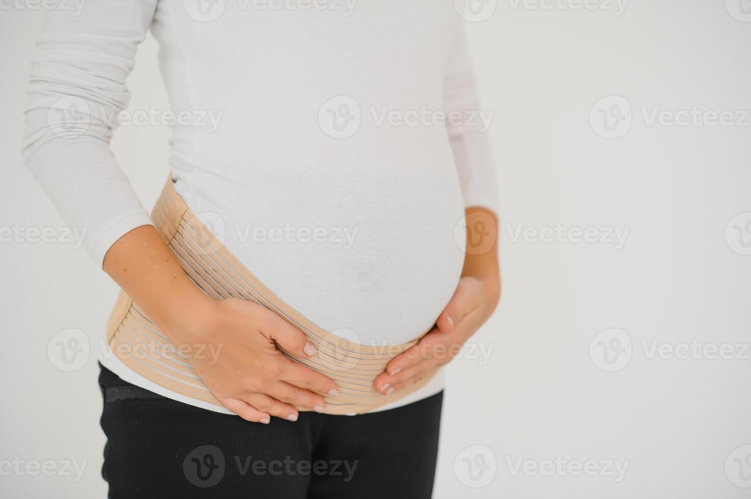 fechar acima do grávida mulher colocando em uma curativo às cinzento fundo com cópia de espaço. ortopédico abdominal Apoio, suporte cinto conceito. foto