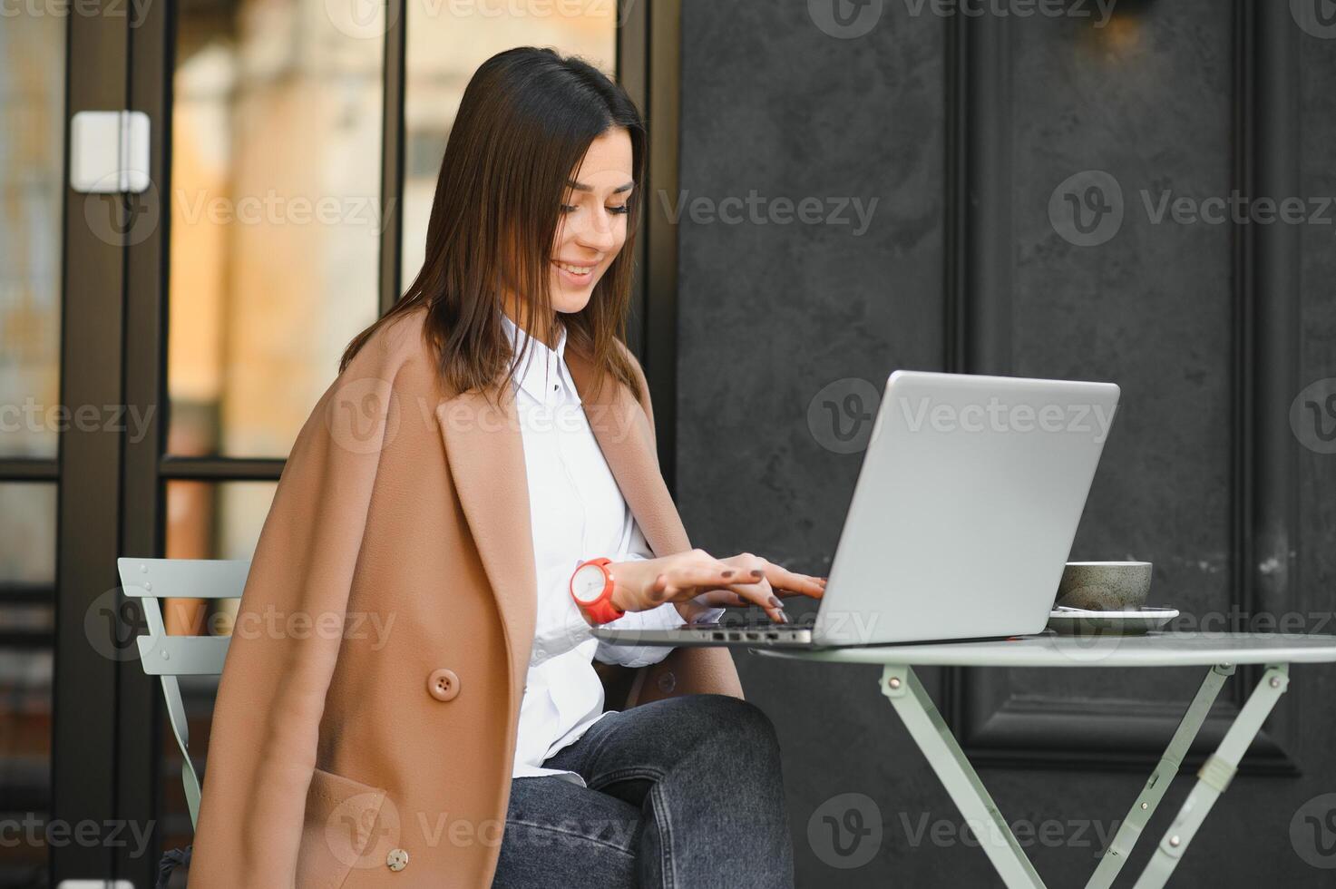 jovem trabalhador autonomo mulher desfrutando café enquanto trabalhando ao ar livre em uma computador portátil computador conectado para público Wi-fi. à moda aluna menina estudando conectados dentro cidade. foto